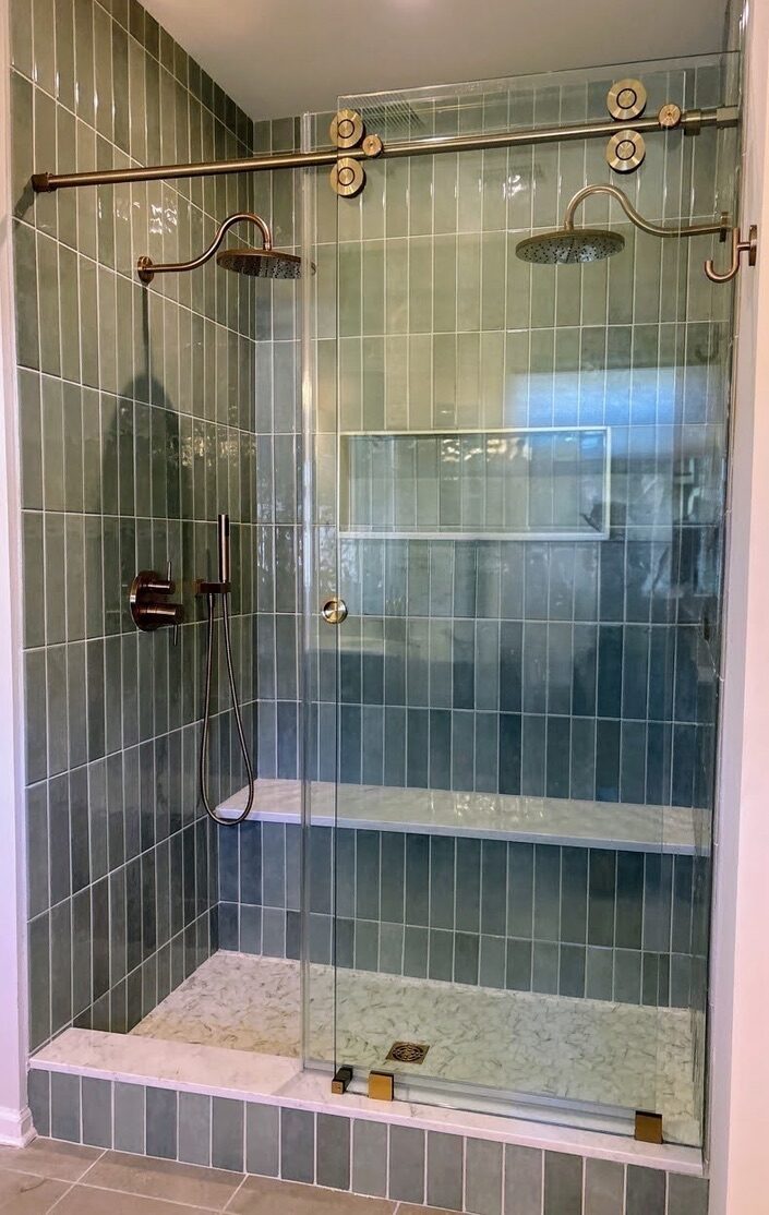 Walk-in shower with green vertical tile, dual rain shower heads, and brushed gold glass door